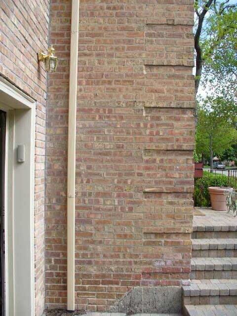 Brick exterior wall beside a doorway and stone steps leading to a patio garden.