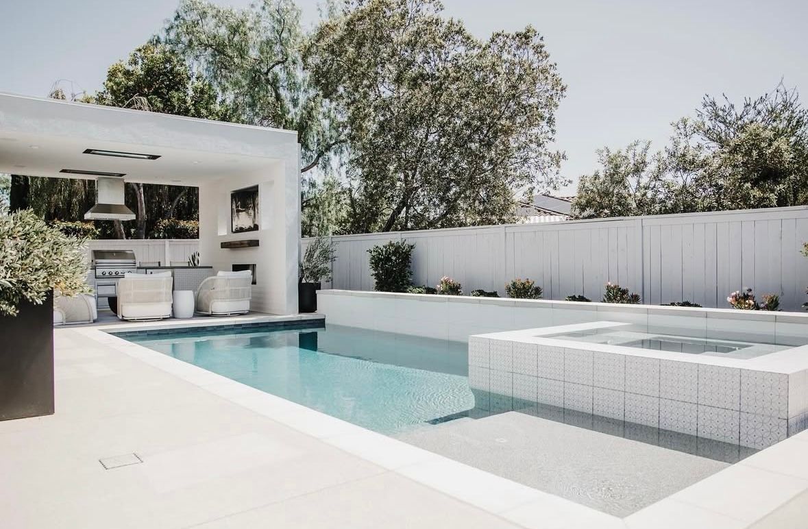 An in ground pool with a white color scheme, jacuzzi, and out door kitchen.