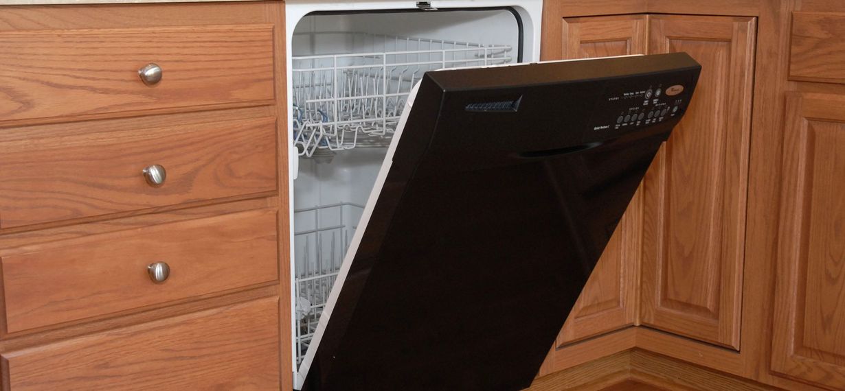 Open dishwasher door beside wooden kitchen cabinets, with dishes visible inside.