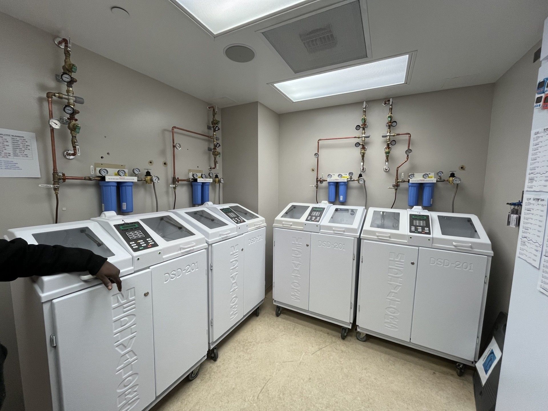 Laundry room with several white washing machines and dryers under bright ceiling lights.