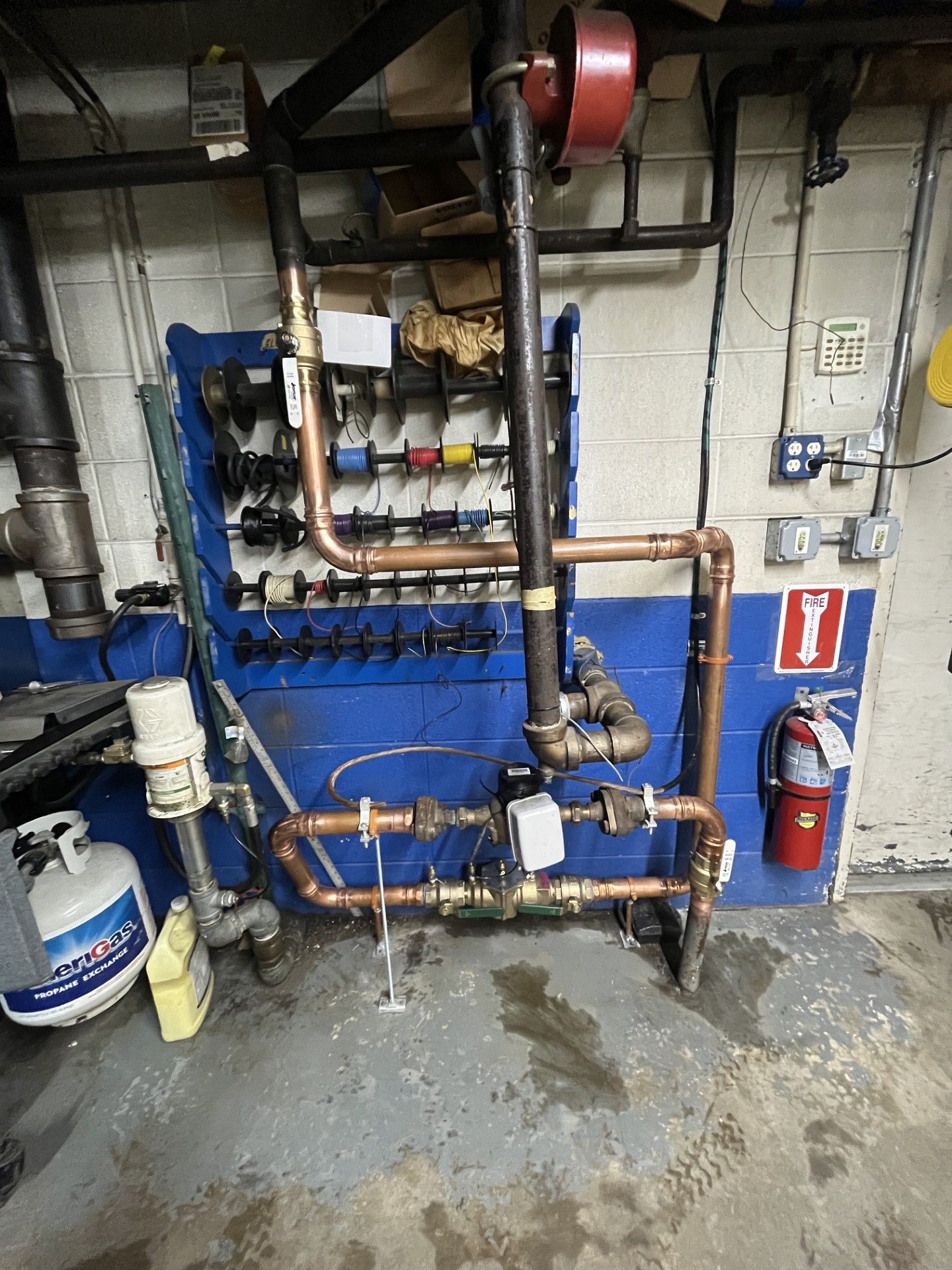 Boiler room with blue heating equipment, copper pipes, gauges, and a wet concrete floor.