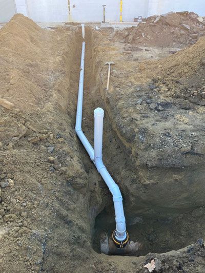 White PVC pipe runs through a dirt trench at an excavation site.