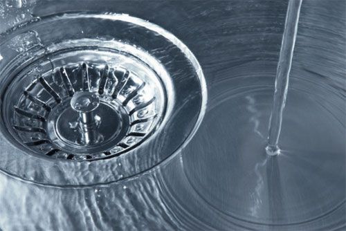 Chrome sink drain with running water and reflections on a metallic surface