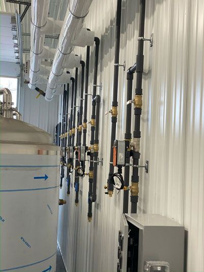 Industrial hallway with wall-mounted pipes, valves, and a gray control box in a white metal building