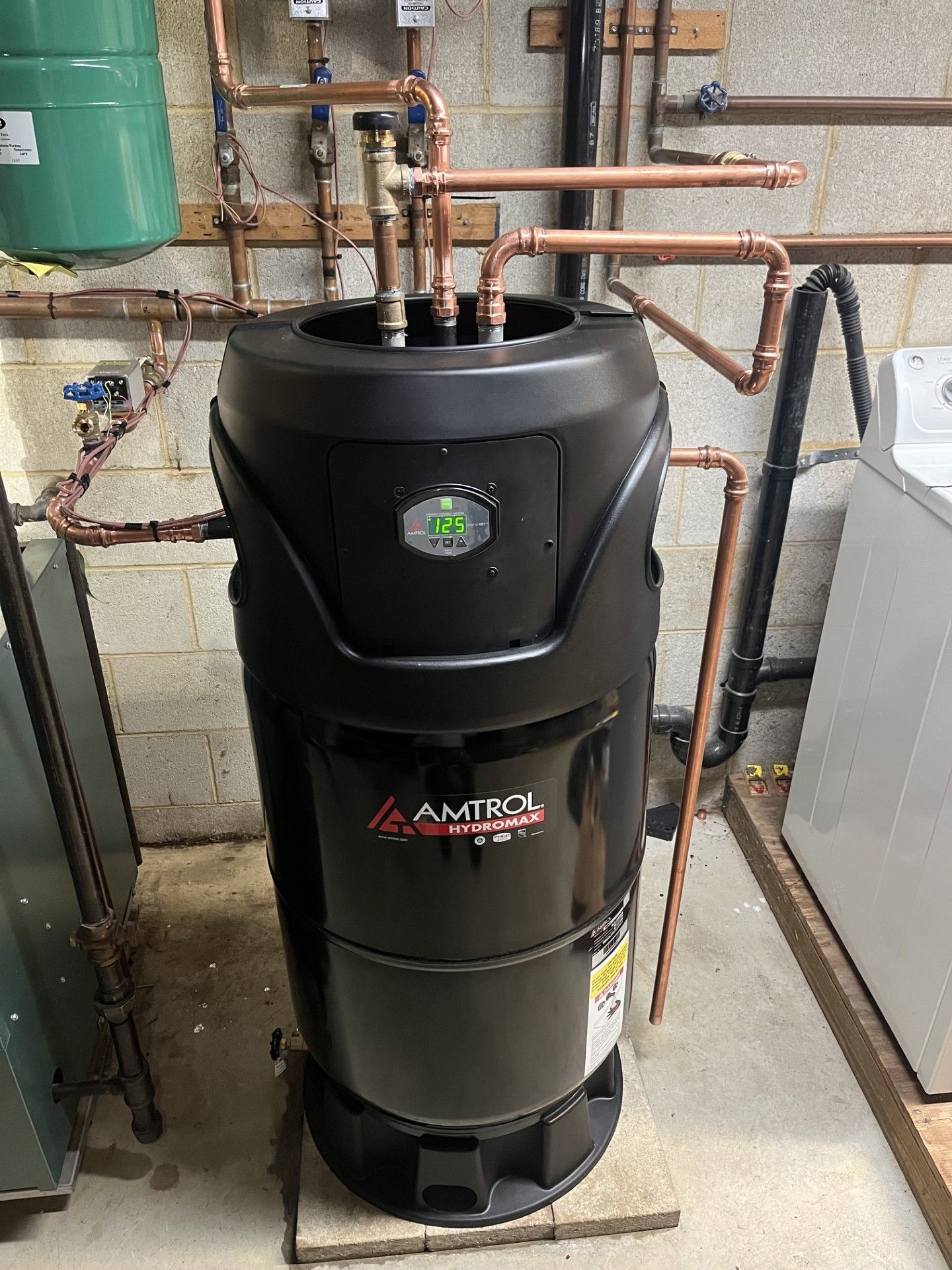 Black A.O. Smith water heater in a basement with copper pipes and a green tank above it