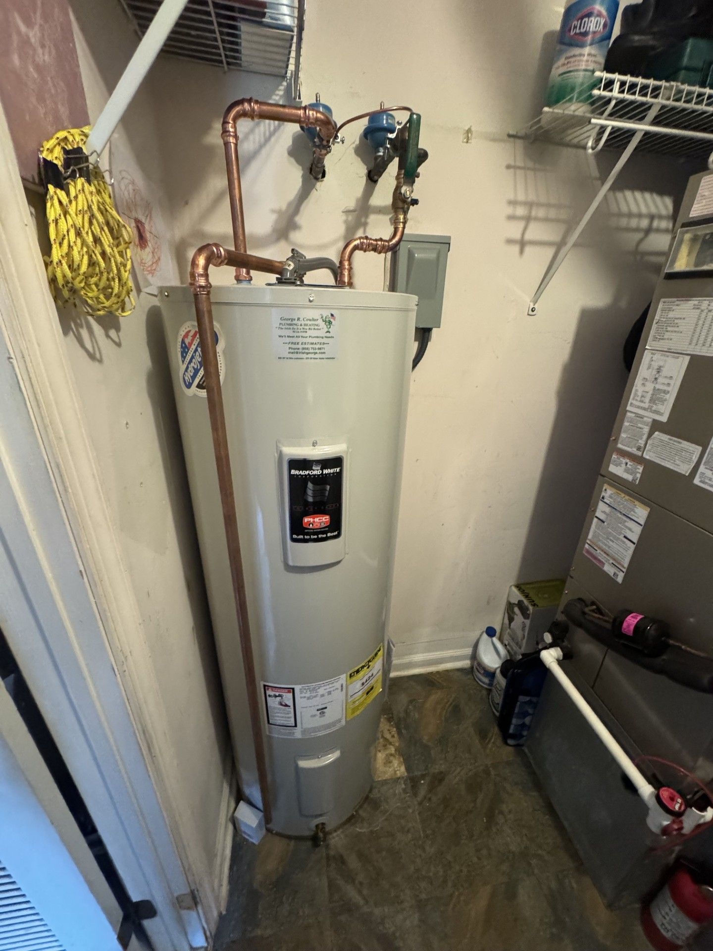 Water heater in a utility closet with exposed copper pipes and storage shelves above.