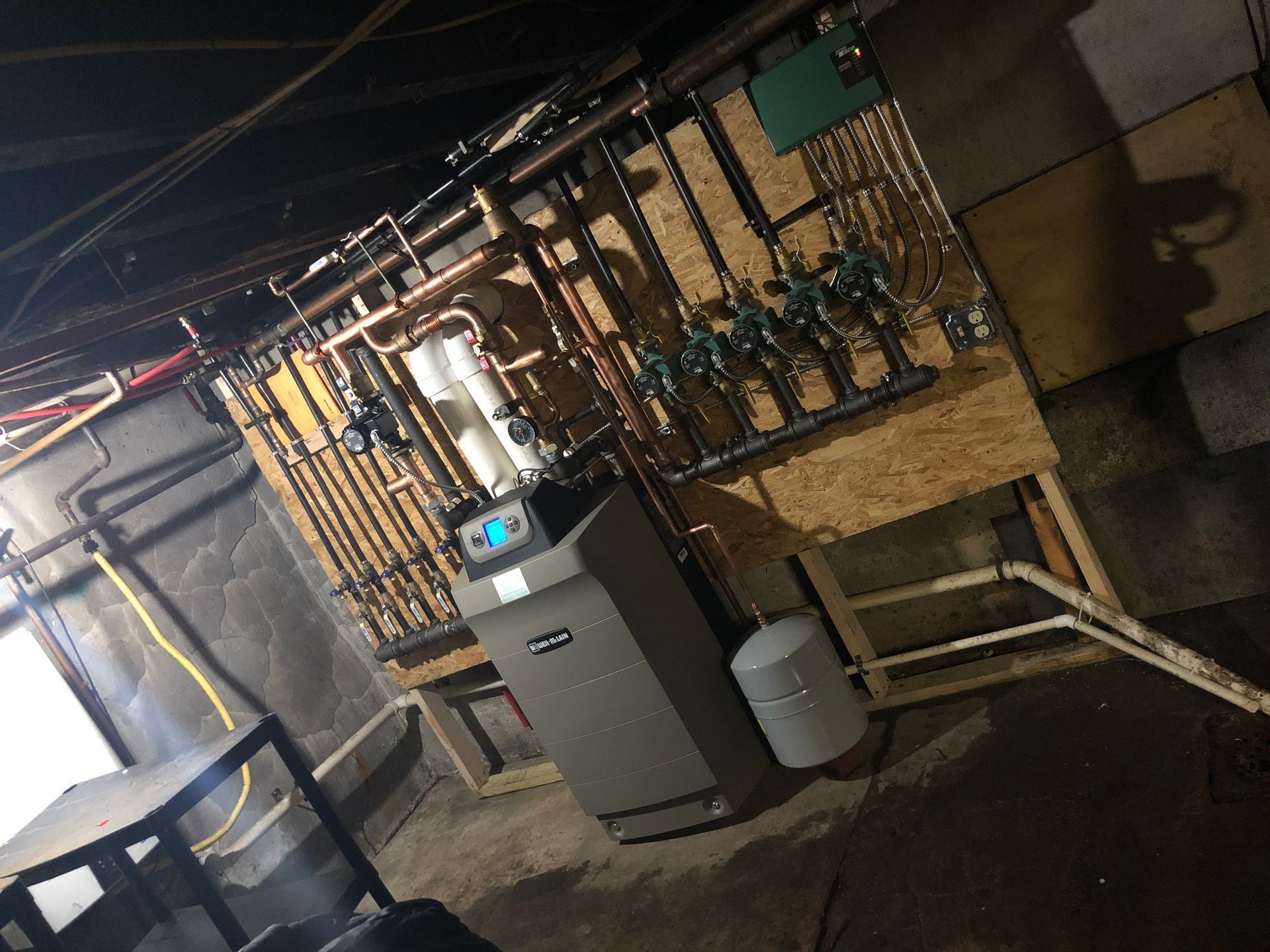 Basement utility room with furnace, water heater, and exposed pipes under fluorescent lighting