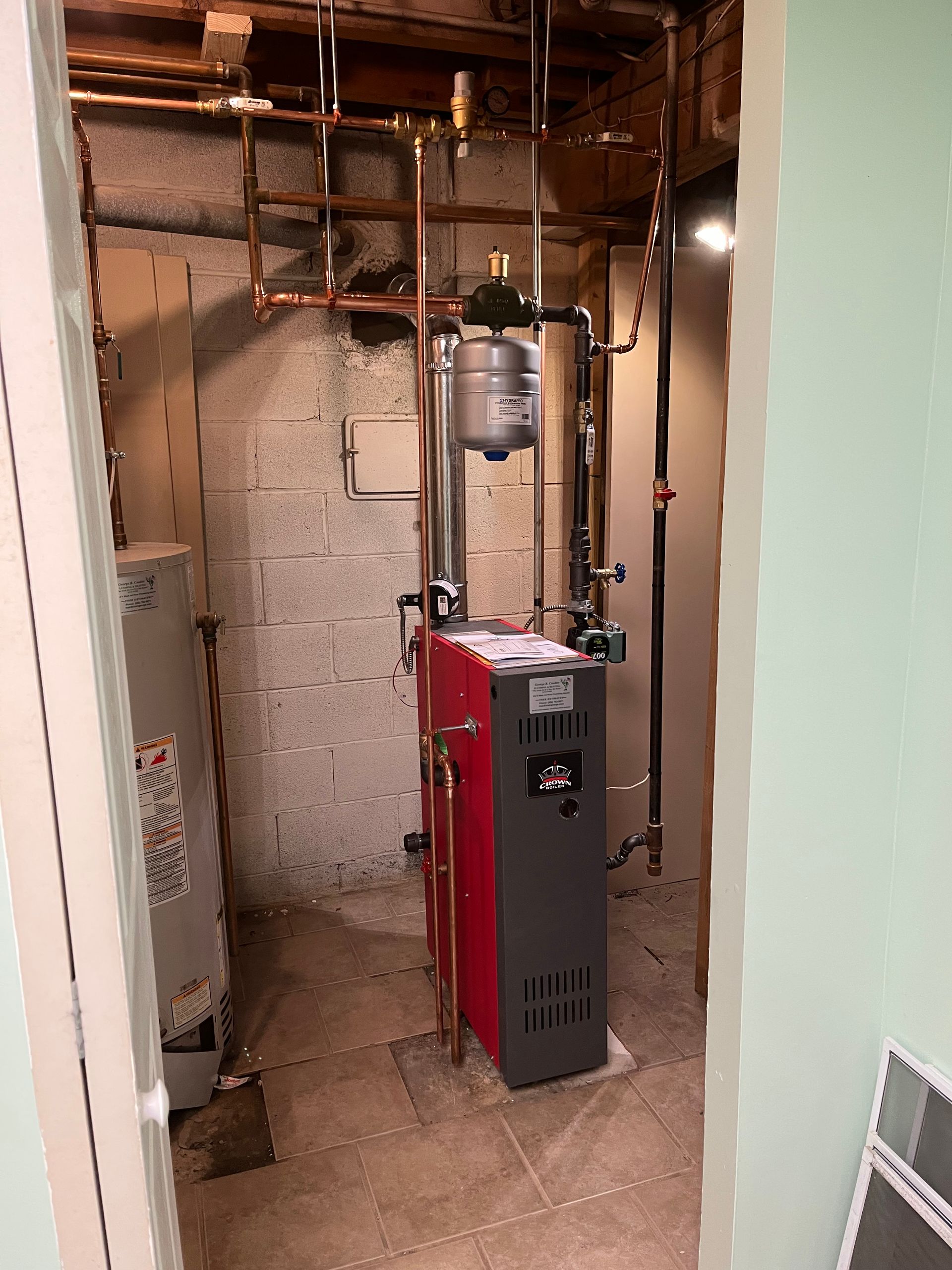 Utility room with a red and black furnace, exposed pipes, and unfinished walls and ceiling.