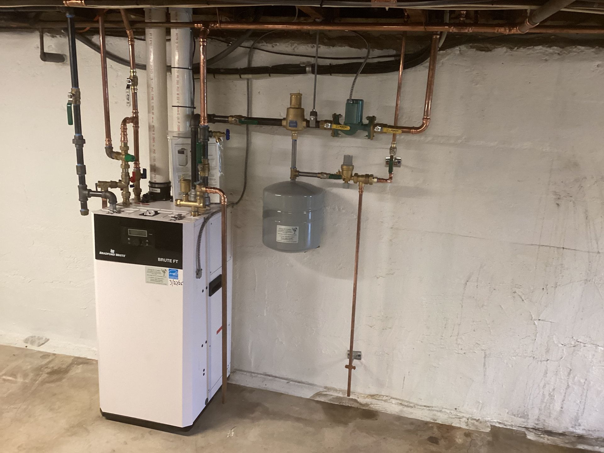 Basement utility room with a white boiler, exposed copper pipes, and wall-mounted water tank