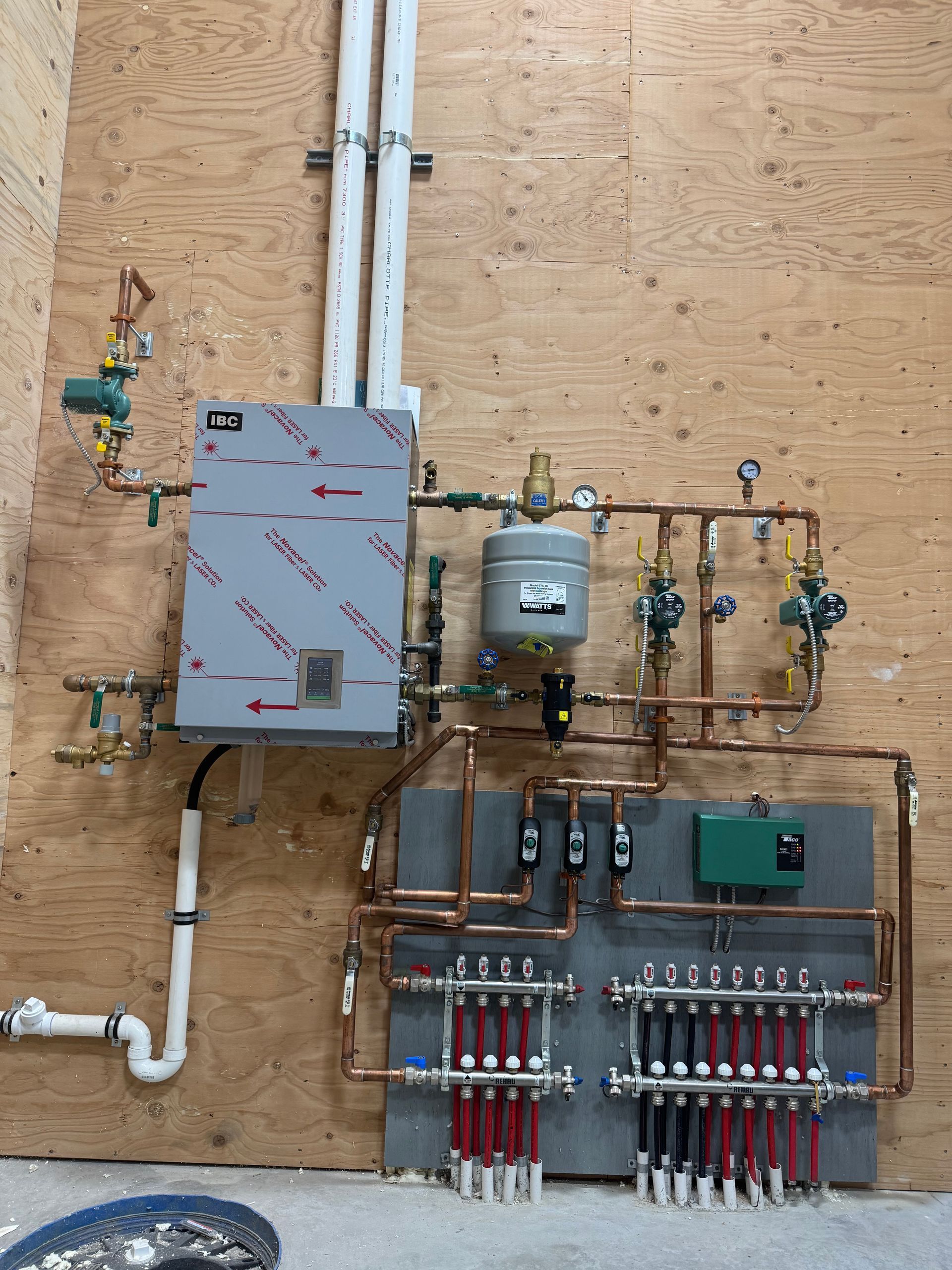 Plumbing and electrical system mounted on a plywood wall with valves, gauges, pipes, and wiring panels.