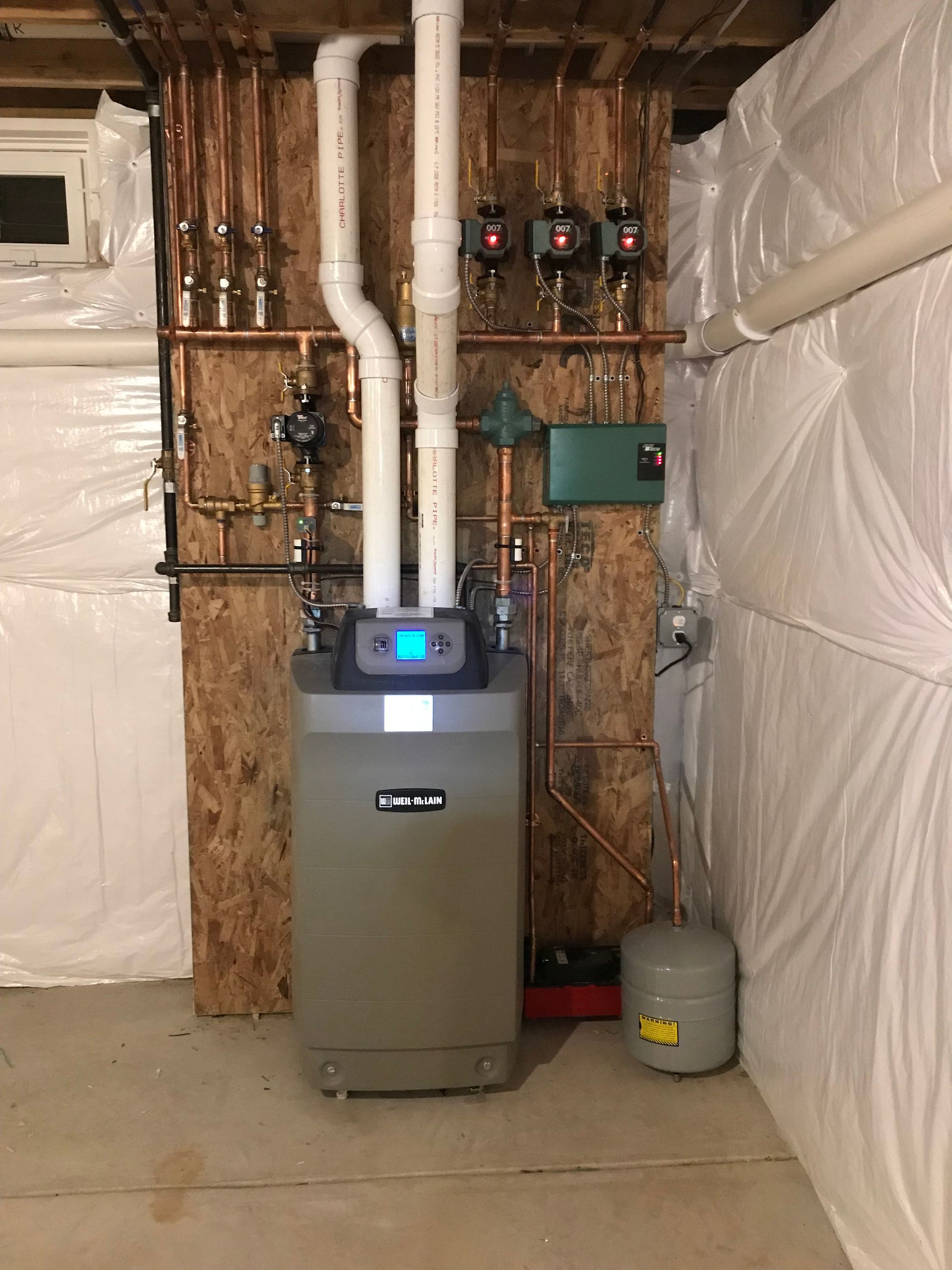 Basement HVAC and boiler system with exposed pipes, furnace, and plastic-covered walls.