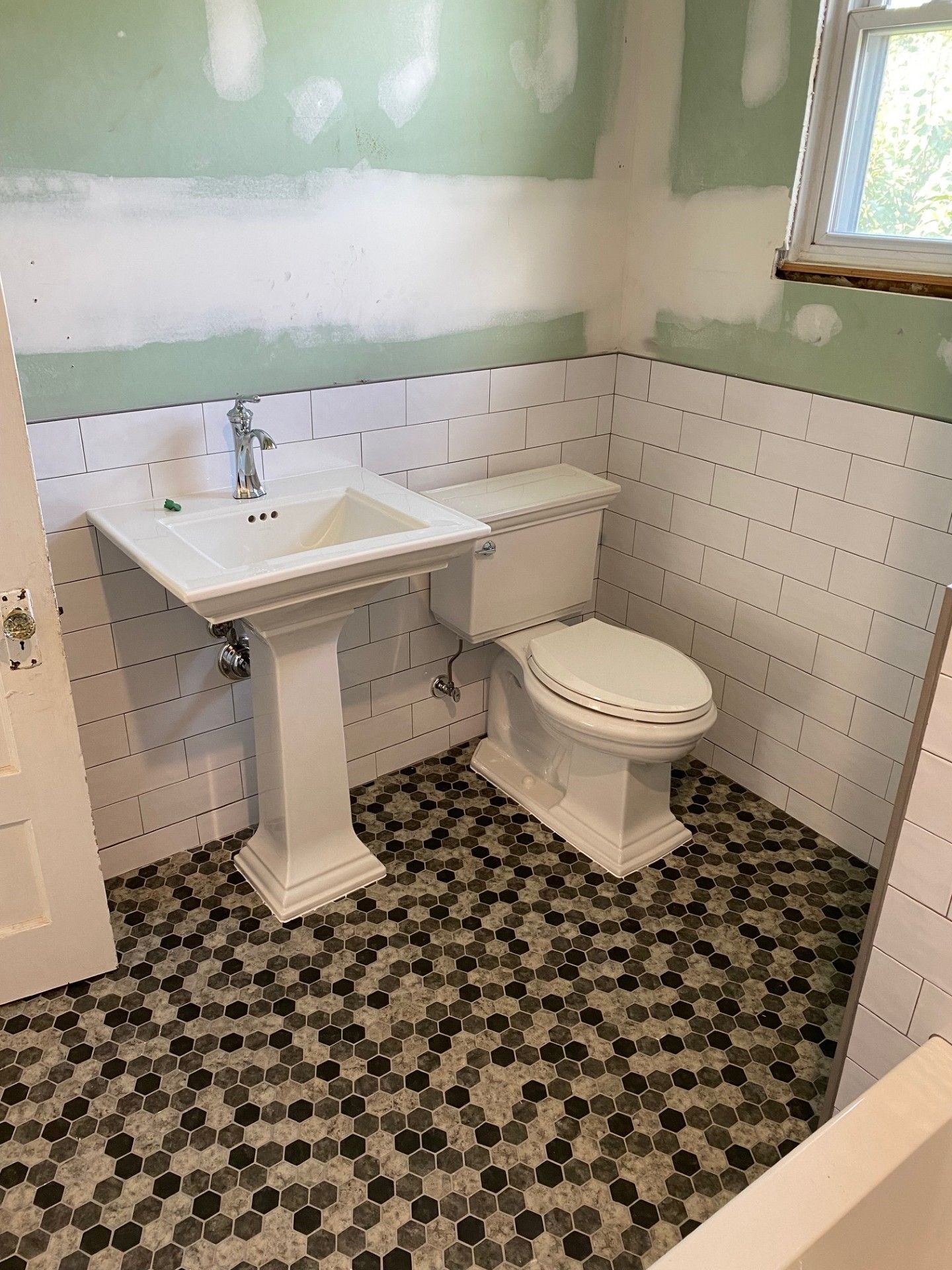 Small bathroom with pedestal sink, toilet, and black-and-white patterned tile floor.