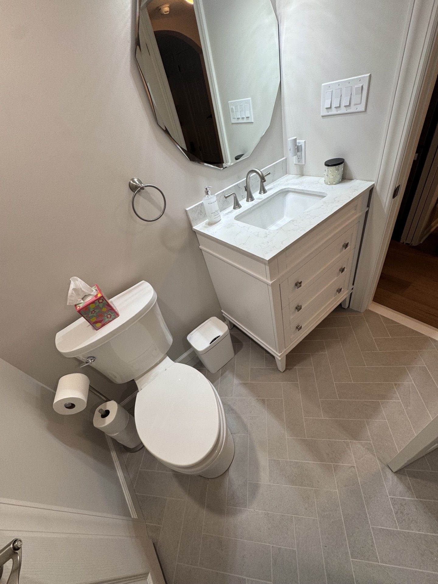 Small bathroom with toilet, sink vanity, oval mirror, and gray tiled floor.