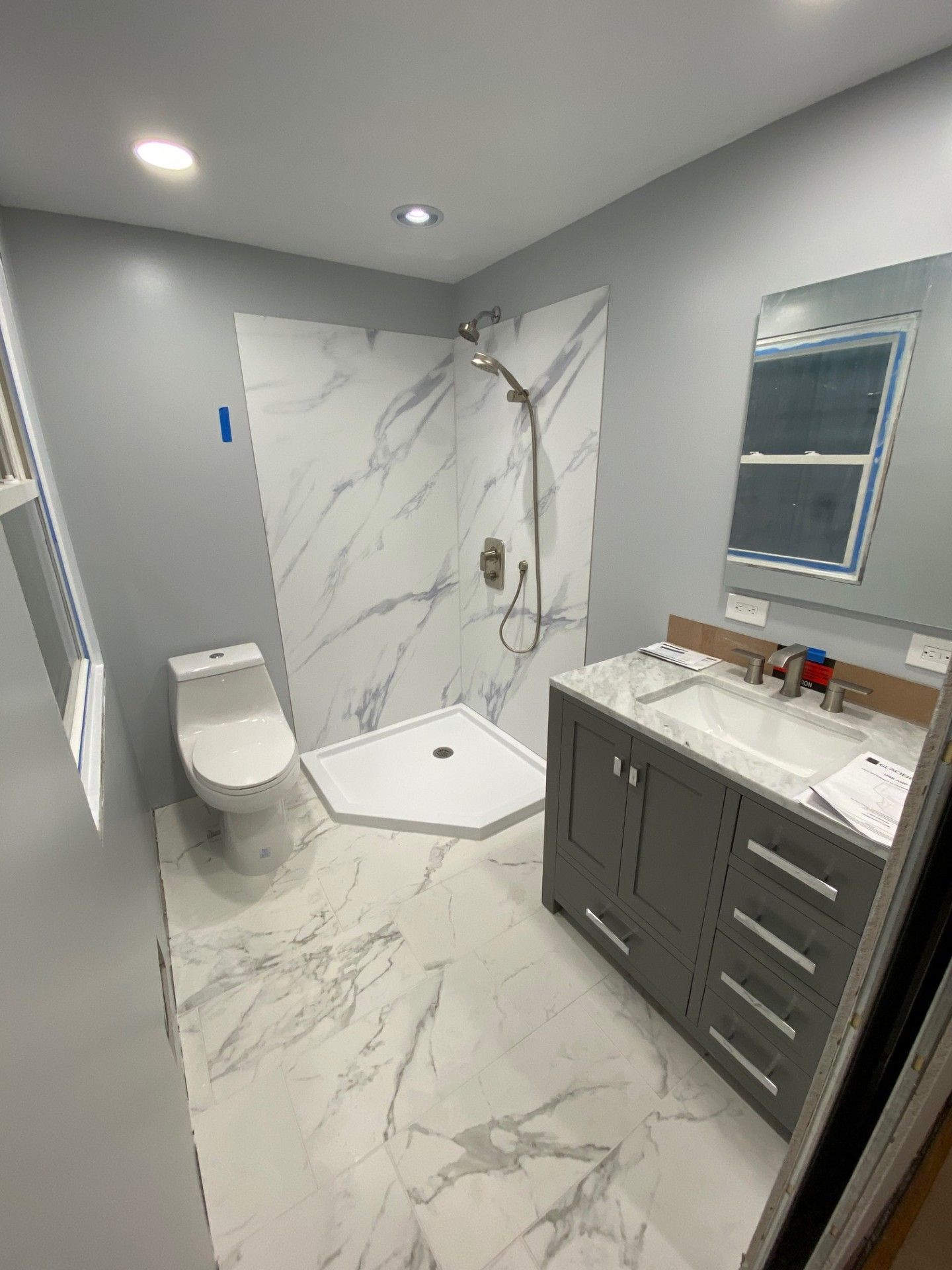 Modern gray bathroom with marble-look tile, shower, toilet, and dark vanity with mirror