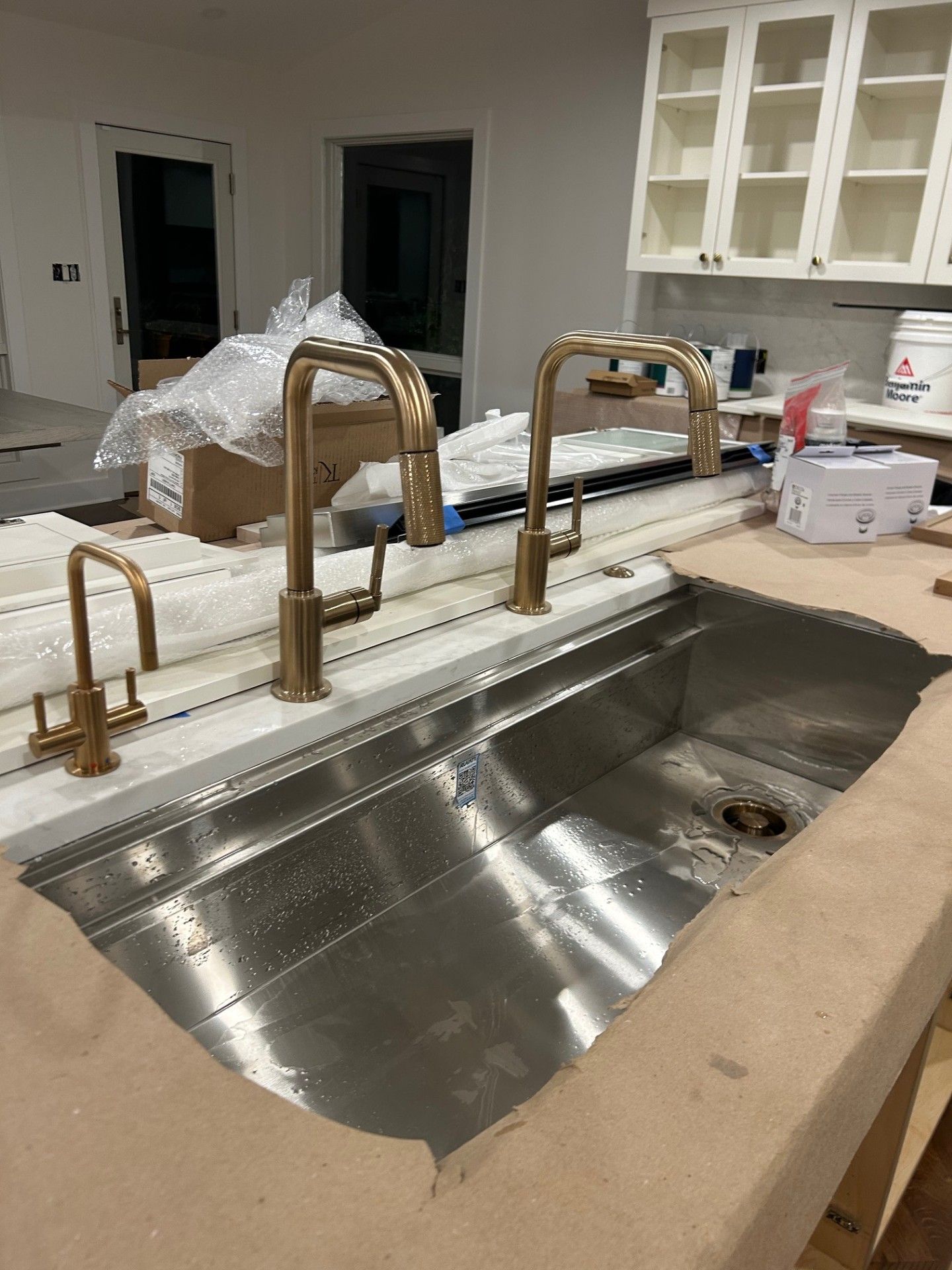 Kitchen sink under construction with stainless steel basin, gold faucets, and unfinished countertop
