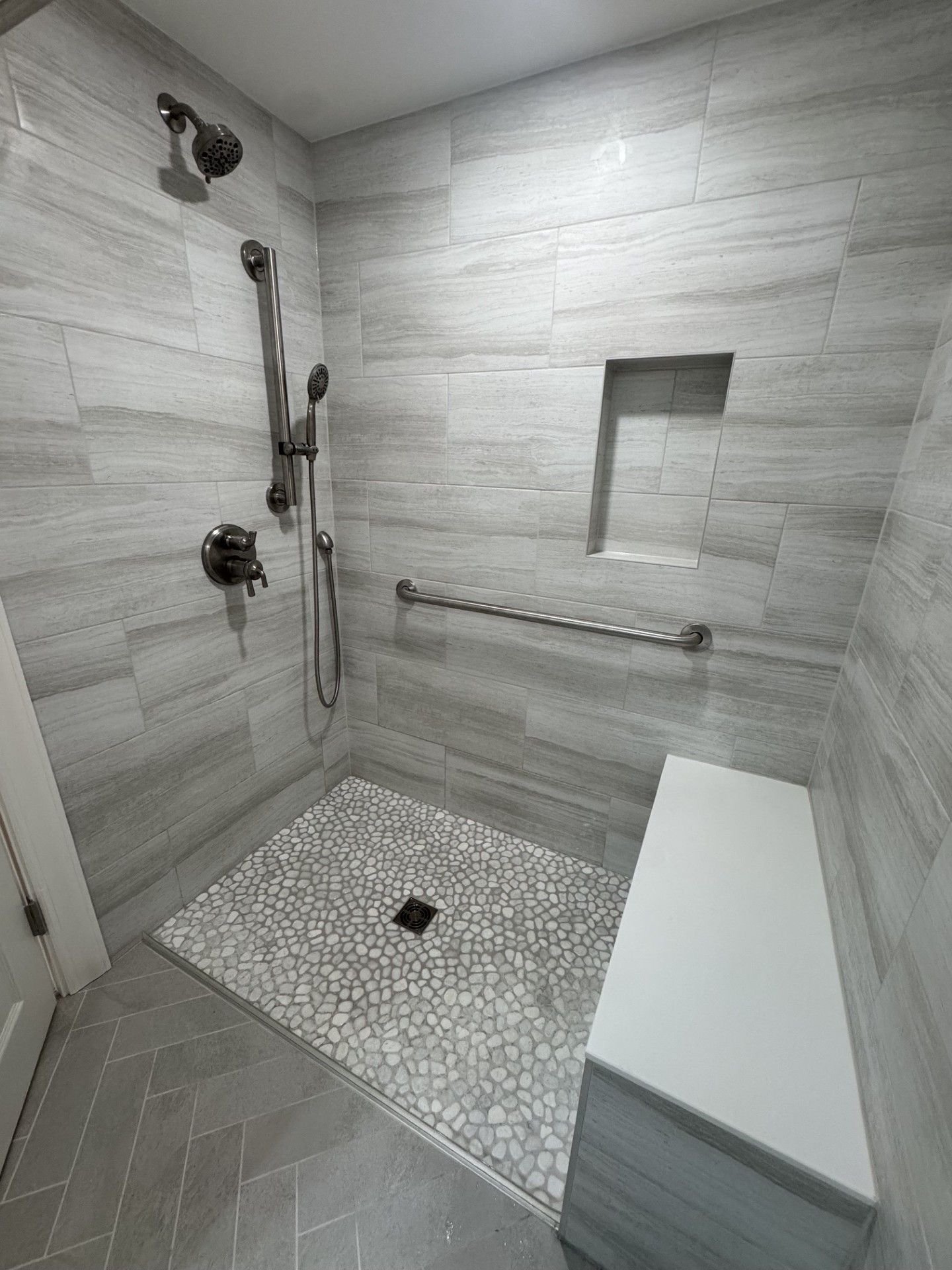Accessible shower with grab bars, bench, handheld showerhead, and mosaic tile floor