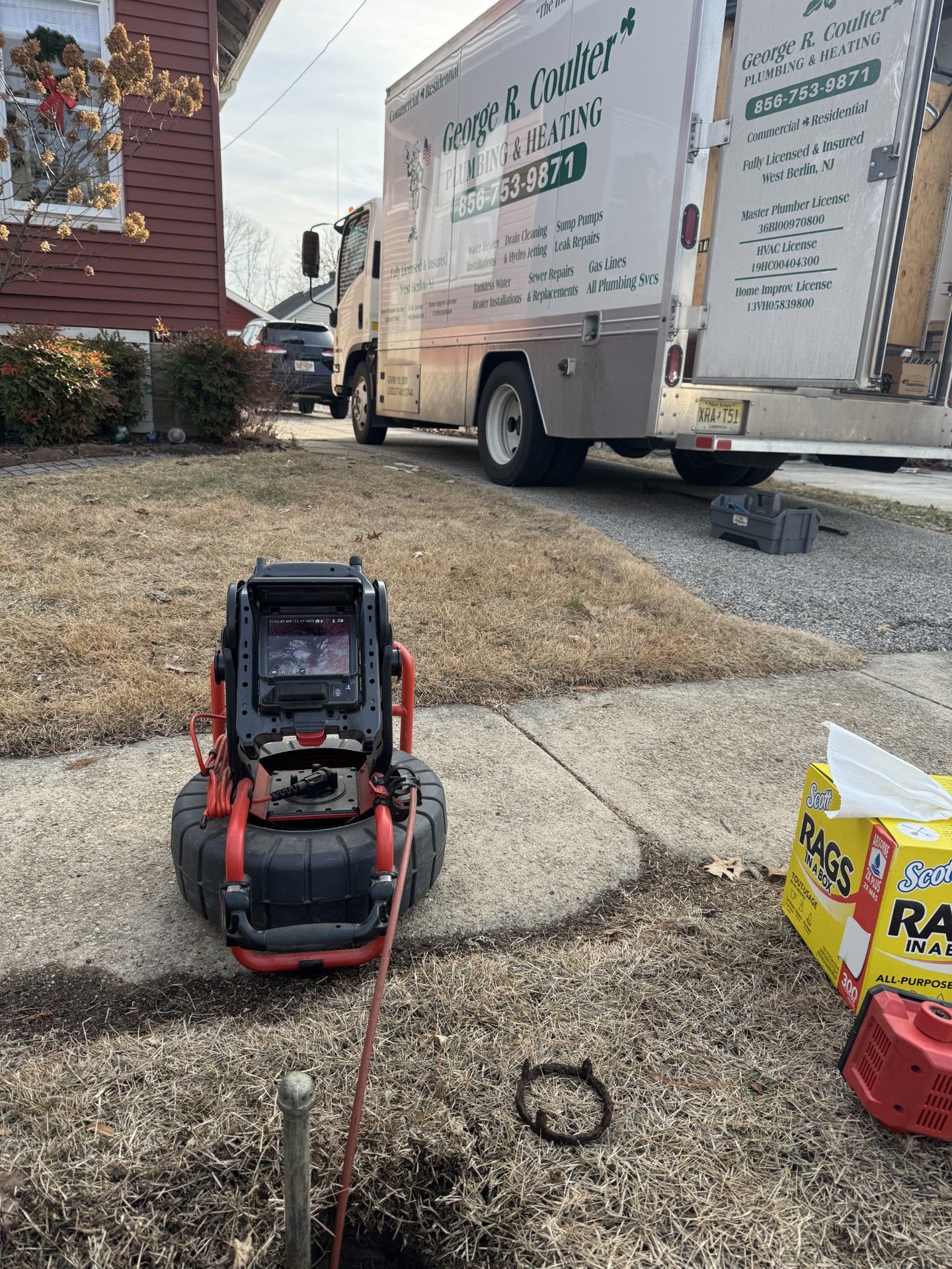 Red-and-black lawn machine on sidewalk beside a moving truck and yard supplies in a residential driveway