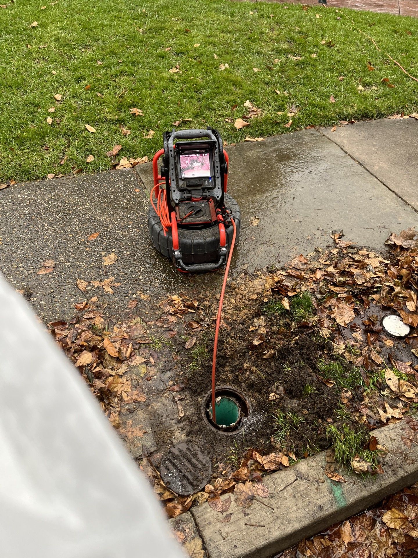Portable drain snake on a wet curbside drain, with red extension cord on the ground.