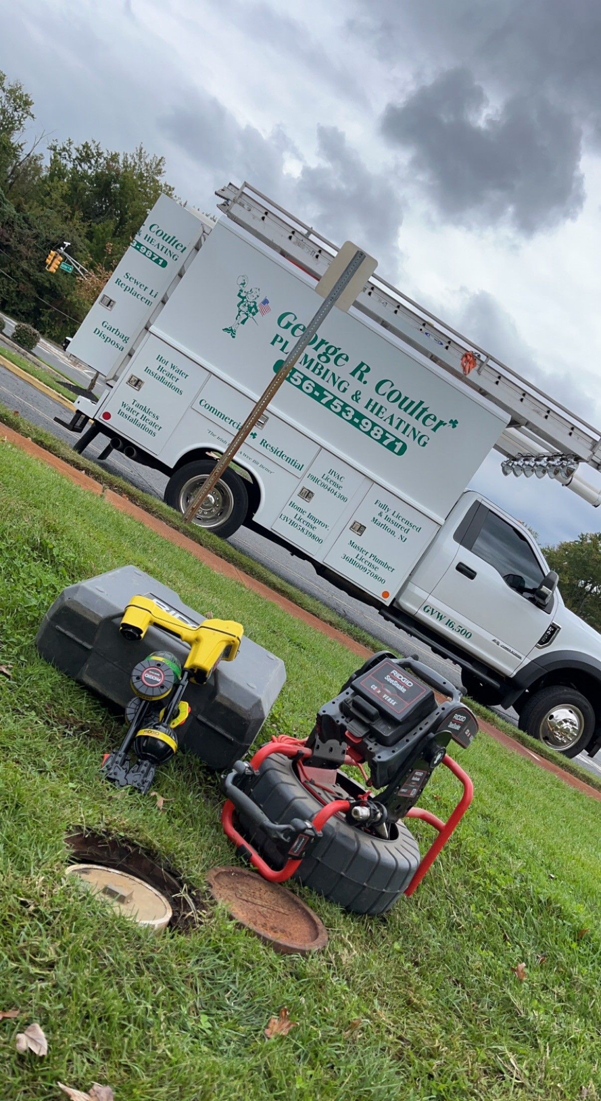Tow-behind lawn mower parked on grass beside a white service truck under cloudy skies.