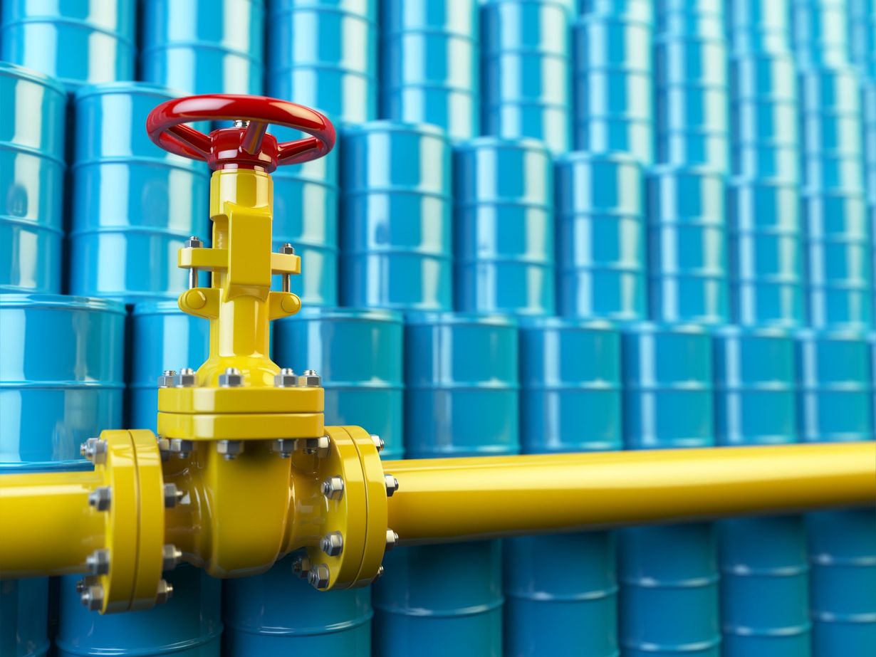 Yellow industrial pipeline valve with a red handwheel against a blue background of stacked barrels