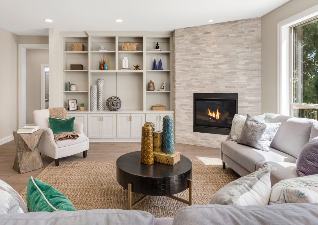 Modern living room with built-in shelves, stone fireplace, gray sofa, white chairs, and round coffee table