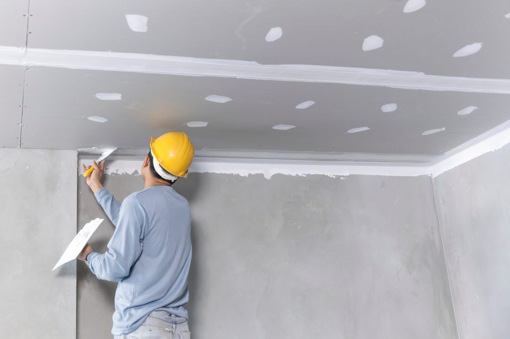 Worker in a yellow hard hat applying drywall compound to a ceiling during interior renovation