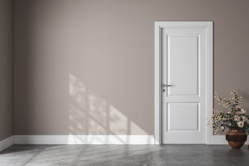 Empty beige room with white door, sunlit wall shadows, and a potted plant on the floor