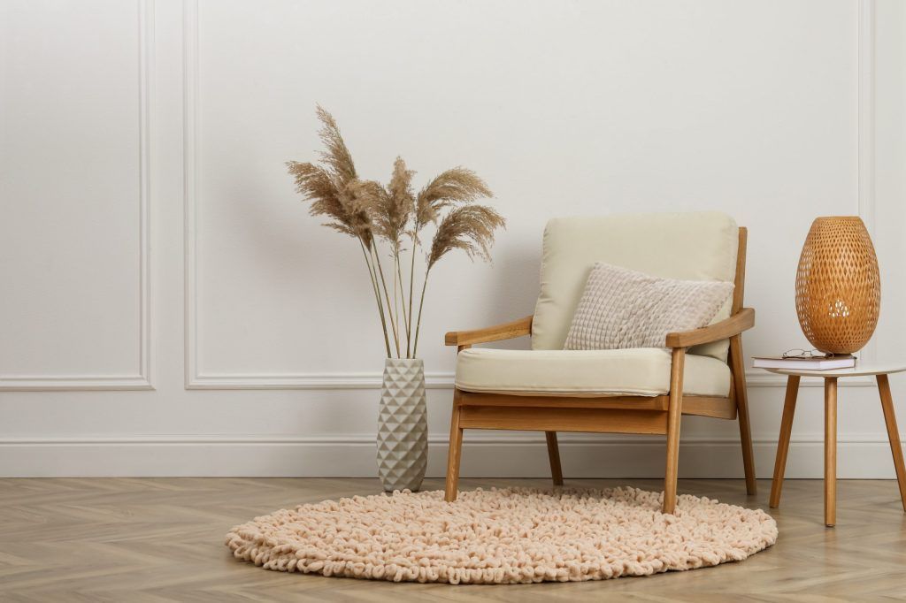 Minimalist living room with beige armchair, round rug, vase of dried grasses, and warm amber lamp