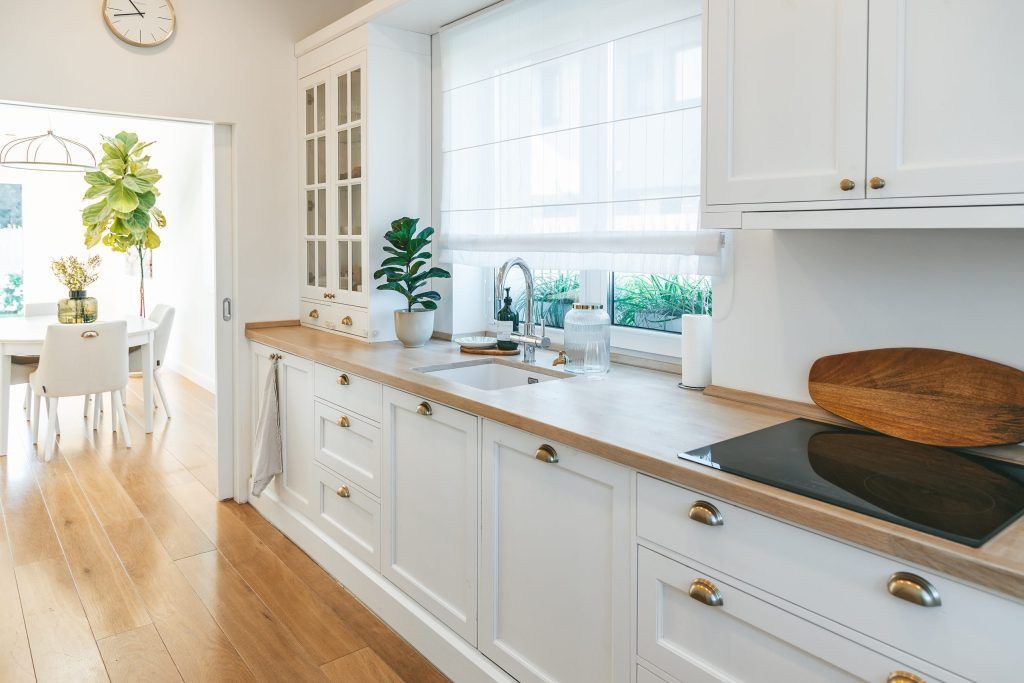 Bright white kitchen with wooden countertops, plants, and a dining area in the background