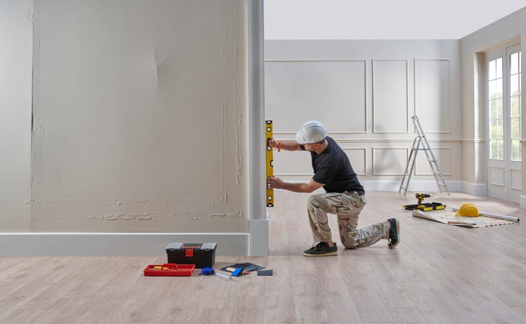 Person kneeling in a bright room, measuring a wall with a level during home renovation