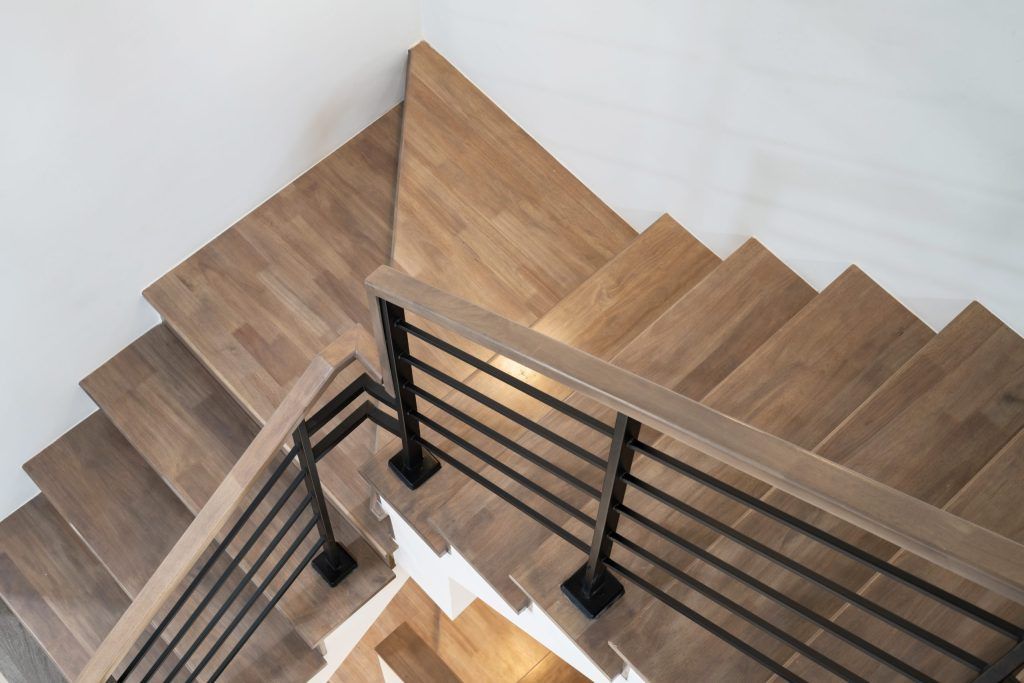 Top-down view of a wooden staircase with black metal railing and light walls