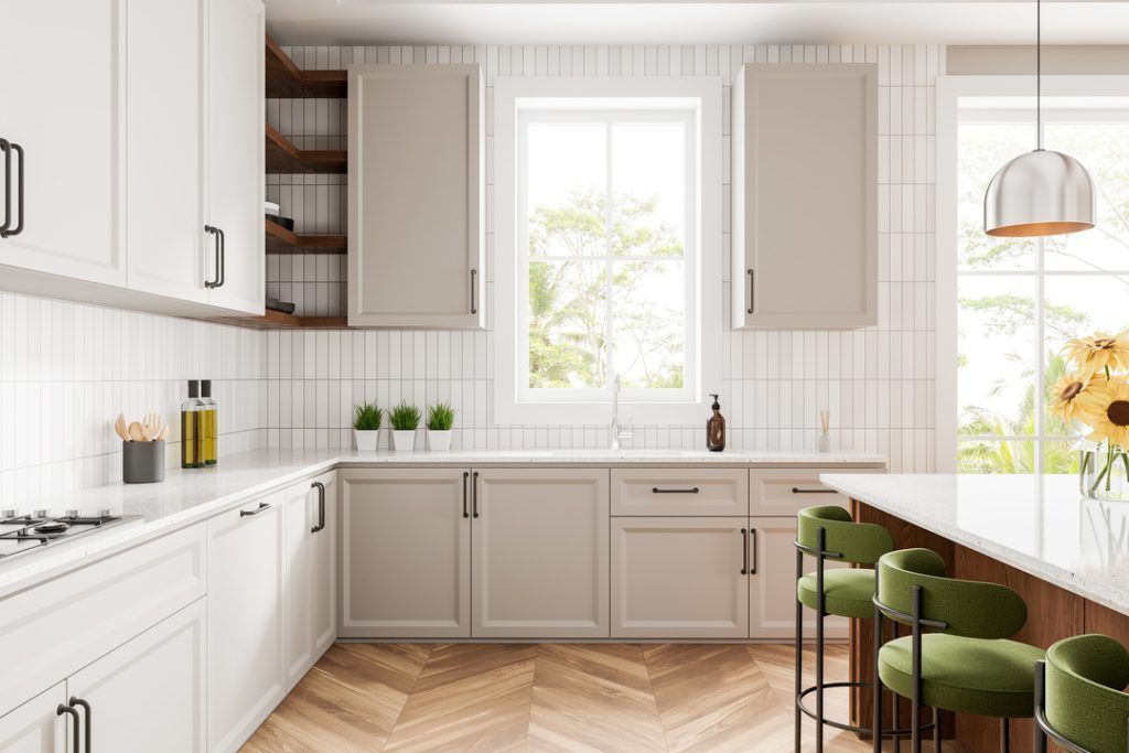 Bright modern kitchen with white cabinets, wood herringbone floor, and green bar stools by a window