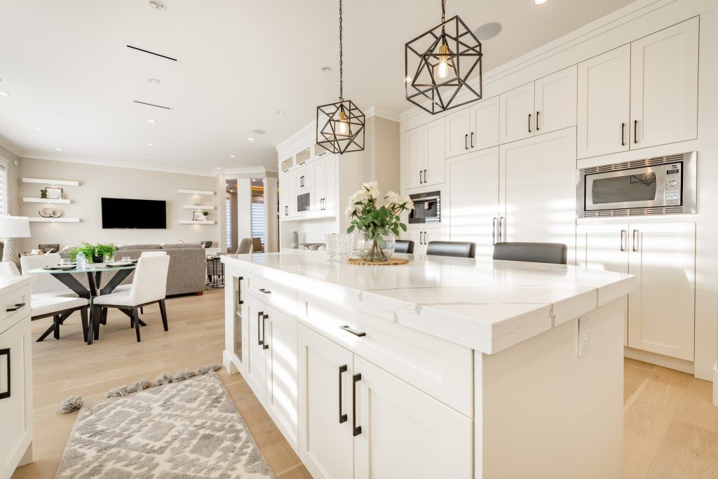 Bright white modern kitchen with island, pendant lights, and adjoining living room with dining table