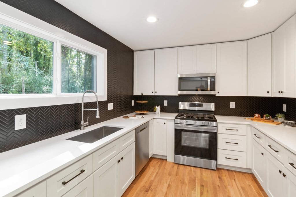 Bright modern kitchen with white cabinets, black countertops, wood floor, and large window over the sink