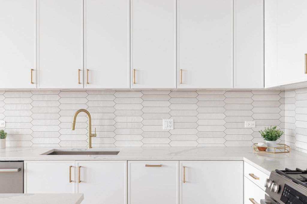 Bright white kitchen with gold hardware, tiled backsplash, and stainless steel appliances