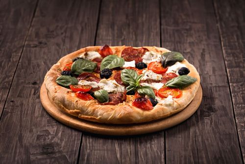 Pizza with basil and tomatoes on a wooden board, on a rustic wooden table.