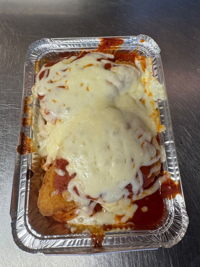 Foil takeout tray of baked pasta covered in melted cheese and red sauce