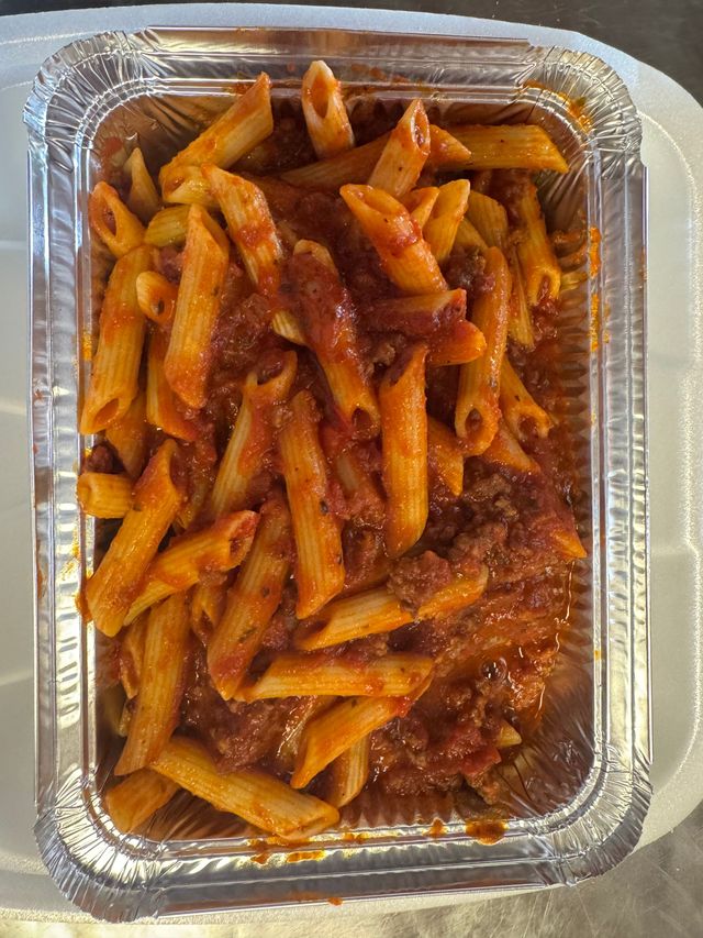Plastic takeout tray of penne pasta in red tomato sauce