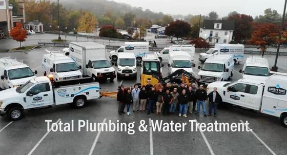 A group of plumbing and water treatment trucks are parked in a parking lot