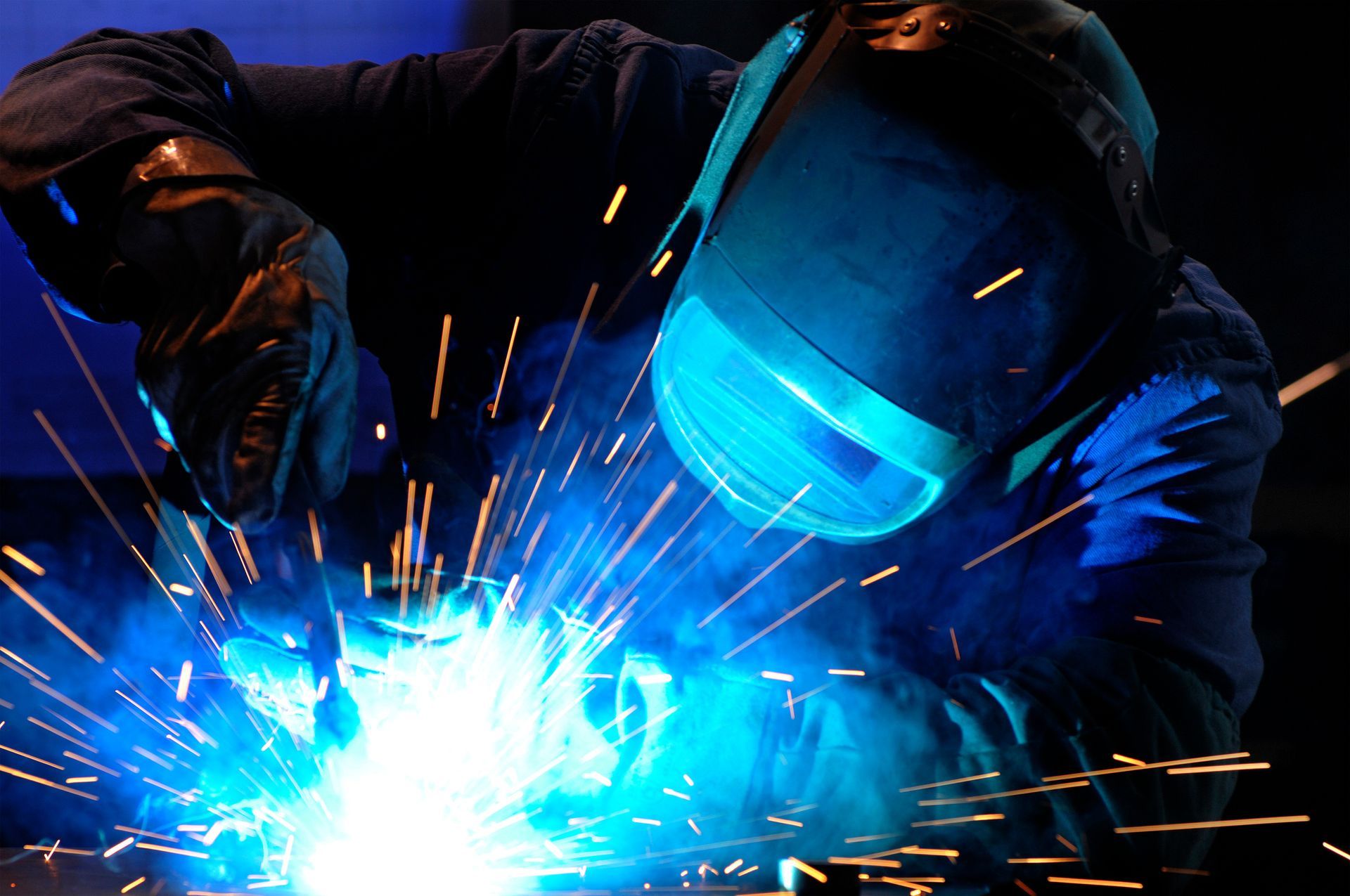 A man wearing a welding mask is welding a piece of metal.