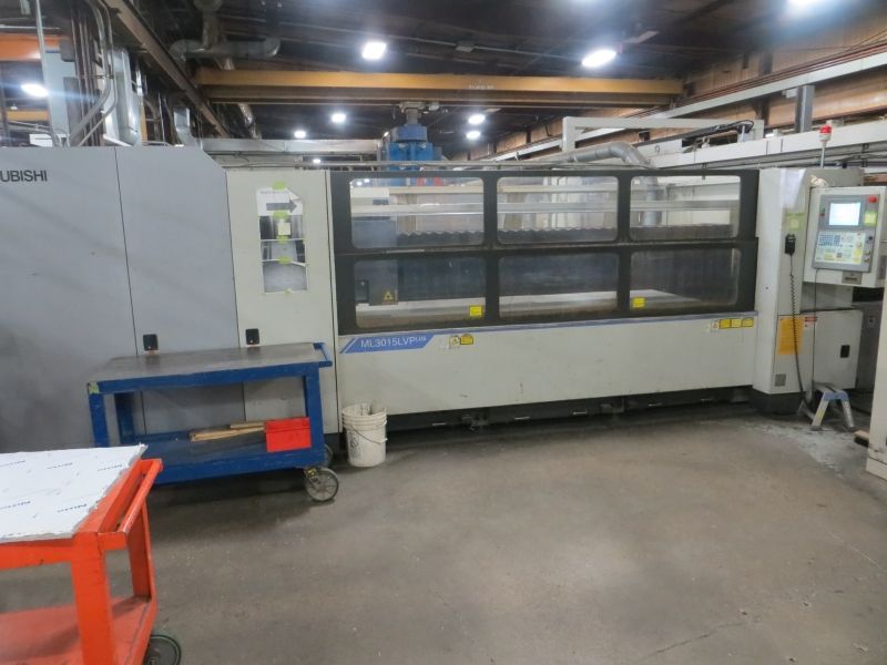 A large machine is sitting in a warehouse next to a cart.