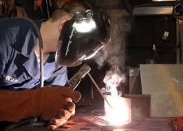 A man wearing a welding helmet is welding a piece of metal.