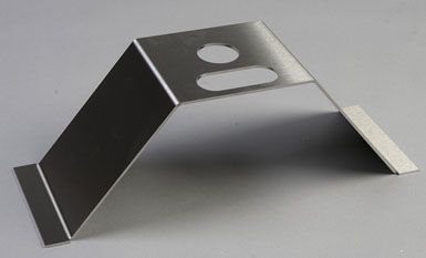 A stainless steel bracket with two holes in it is sitting on a table.