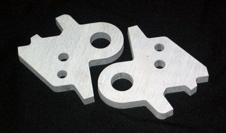 Two pieces of metal with holes in them on a black surface.