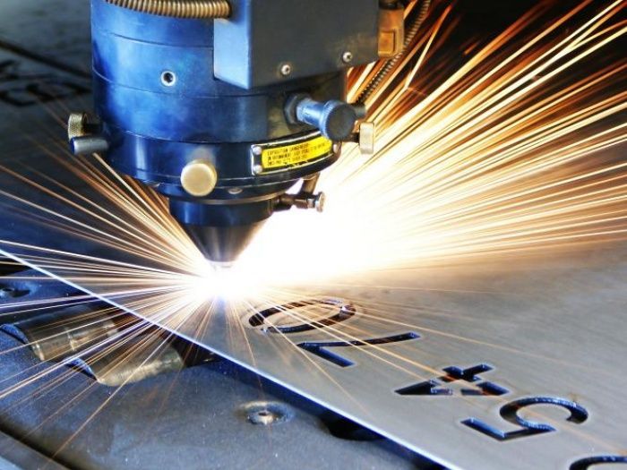 A machine is cutting a piece of metal with the letter g on it.