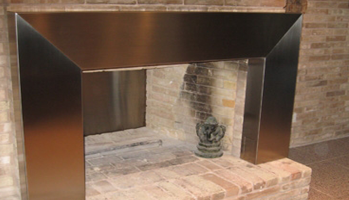 A fireplace with a stainless steel mantle in front of a brick wall.