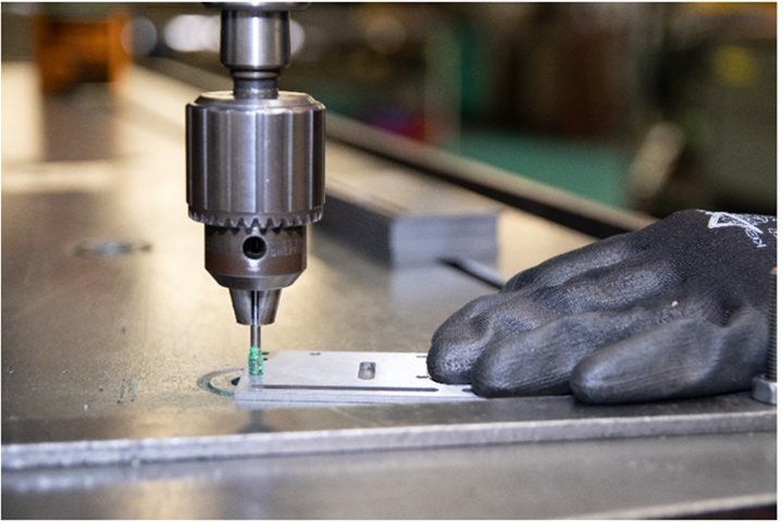 A person is using a drill to drill a hole in a piece of metal.
