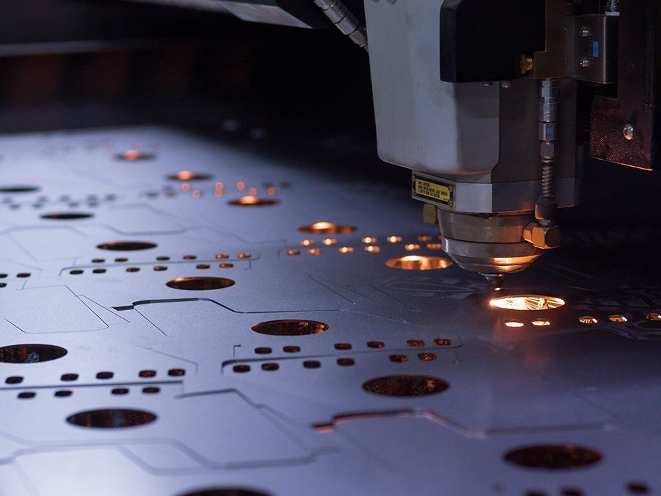A machine is cutting a piece of metal with holes in it.