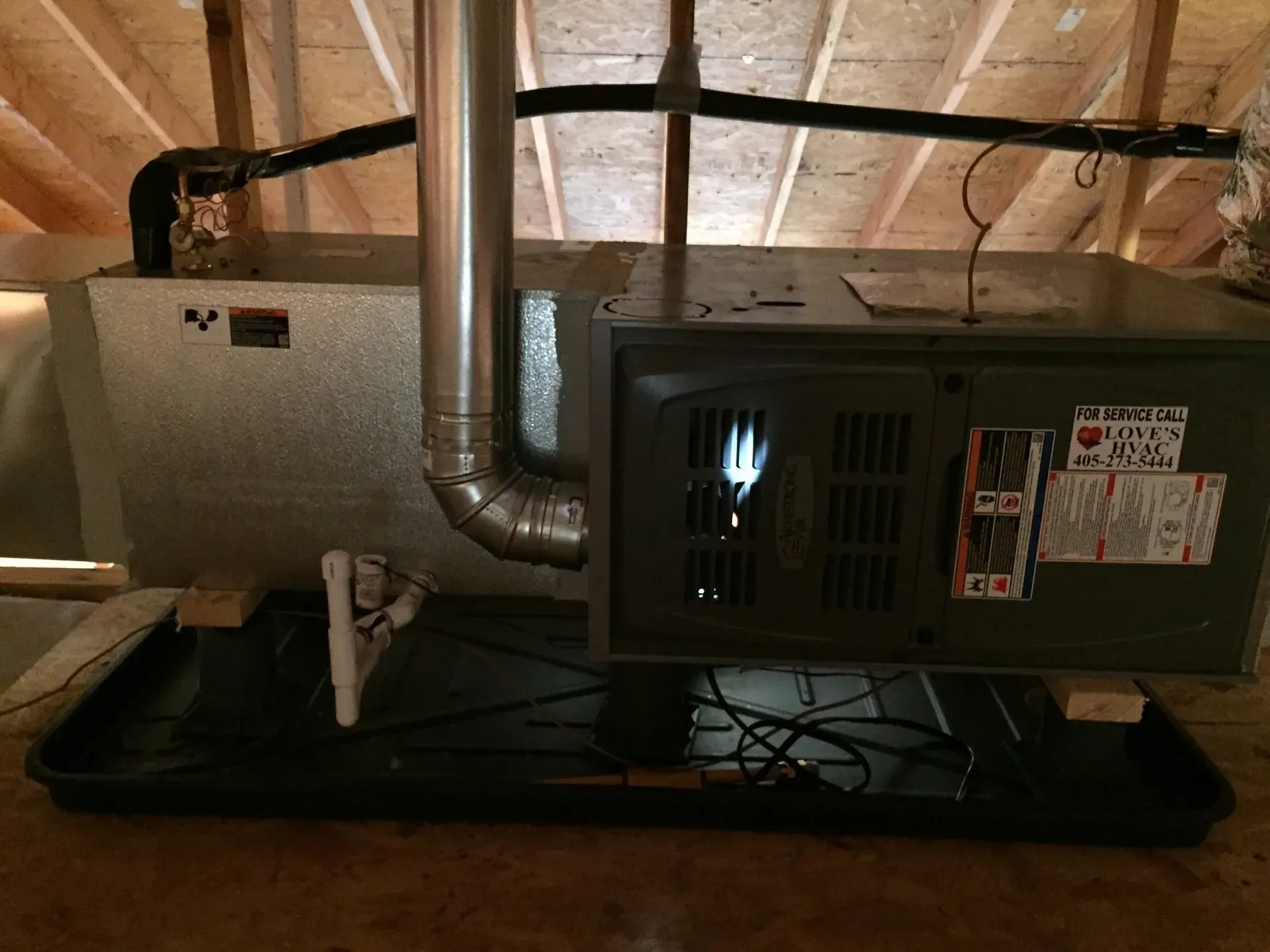 Attic HVAC air handler and ductwork on a black platform beneath exposed wooden rafters.