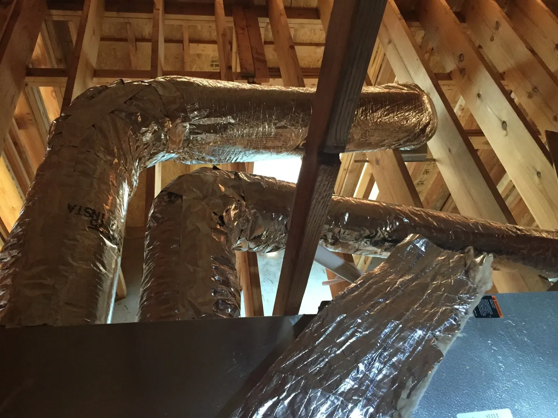 Attic with insulated HVAC ductwork and exposed wooden rafters under roof trusses